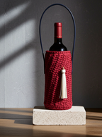 Red wine bottle in a textured red holder with a tassel on a wooden surface.